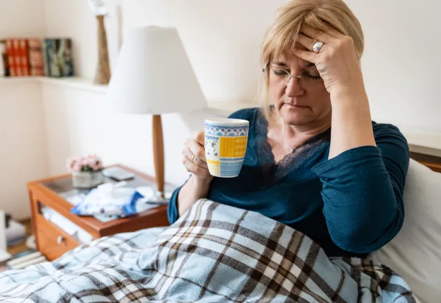 förkyld kvinna med filt i knä och tekopp i handen
